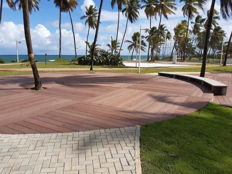 Deck circular em madeira ecológica em praça pública à beira-mar com coqueiros