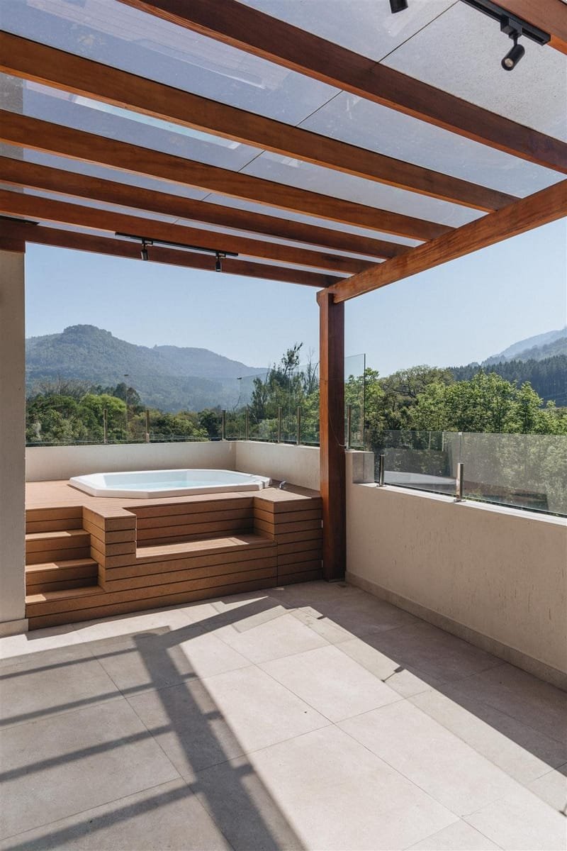 Pergolado com cobertura de vidro sobre deck e spa em terraço com vista para as montanhas