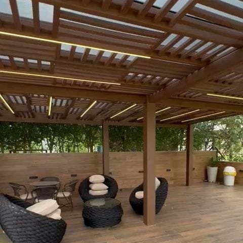 Pergolado Linha Prime cobrindo lounge com poltronas e mesa, com fita de LED entre as vigas