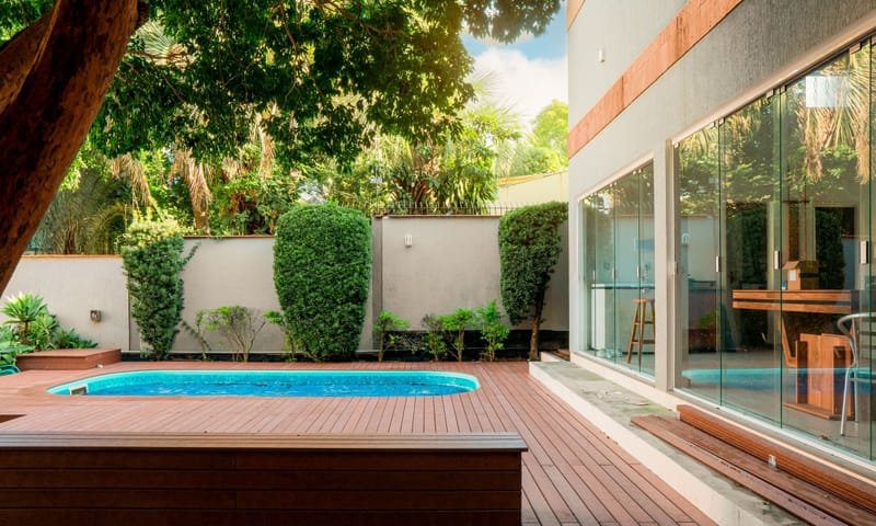 Deck de piscina em madeira ecológica maciça cor Cumaru em quintal com jardim e fachada de vidro